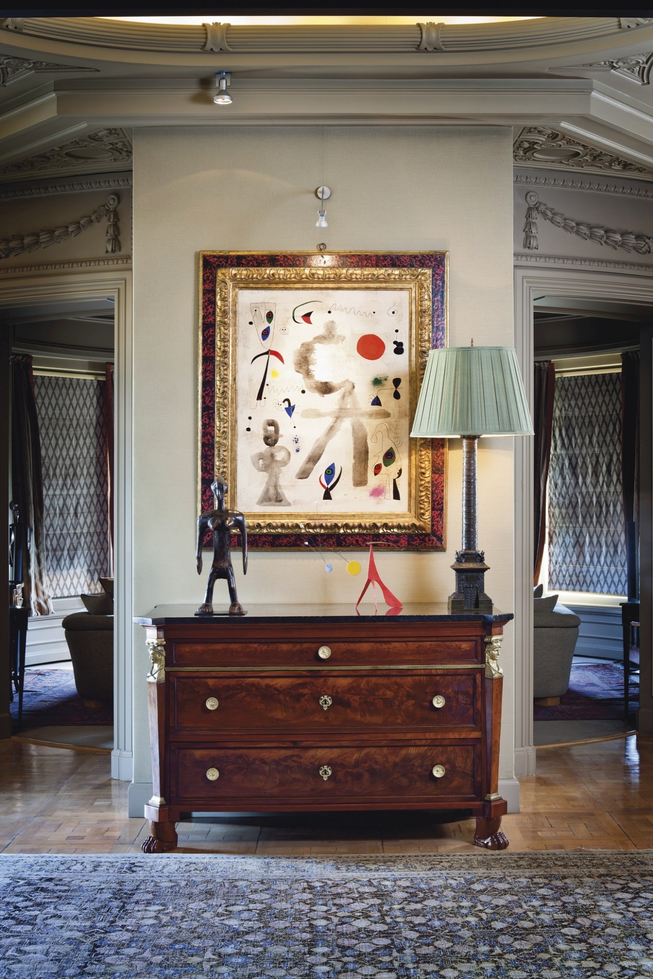 Gallery wall display featuring a framed abstract artwork above an antique wooden dresser with decorative objects and lamp.