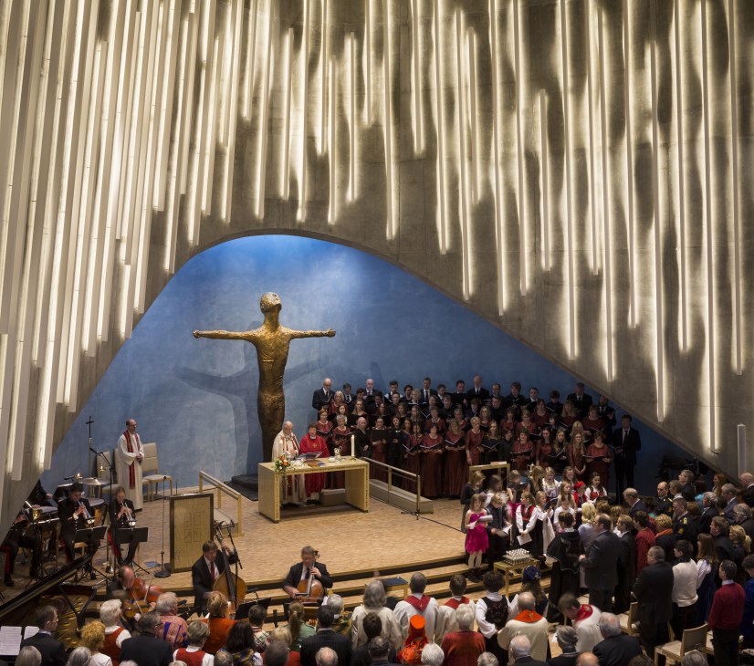 Interior of Cathedral of the Northern Lights in Alta, Norway, showing titanium ribbed ceiling, crucifix, and congregation during service.