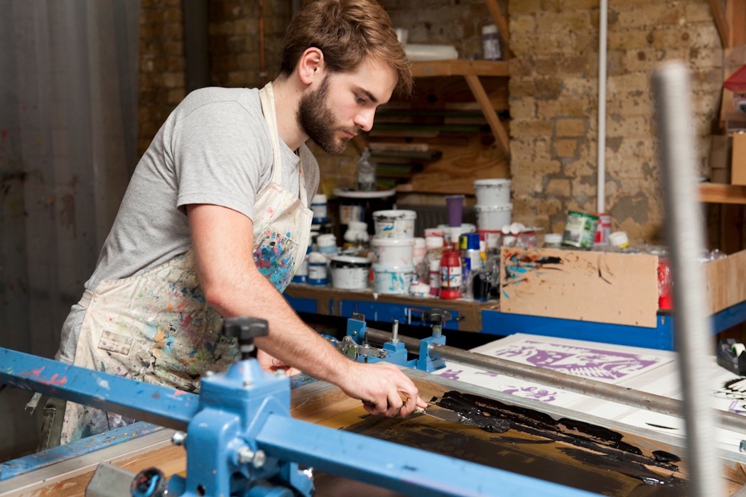 A man in a paint-stained apron operates screen-printing equipment in Nobrow's basement studio.