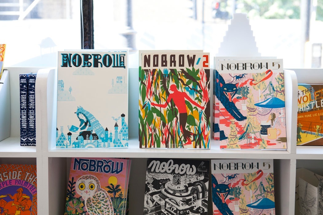 Back issues of Nobrow magazine displayed on white shelves, showing colorful illustrated covers.