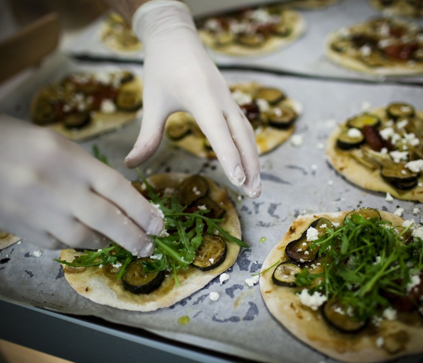 Chef's gloved hand garnishing pizzette with fresh greens and cheese at Rose Bakery.