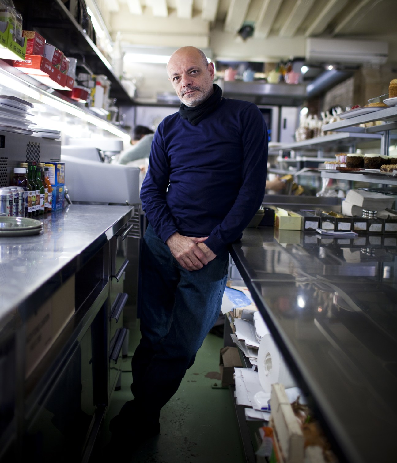 Jean-Charles Carrarini standing in Rose Bakery's kitchen among refrigerated display cases and shelves of ingredients.