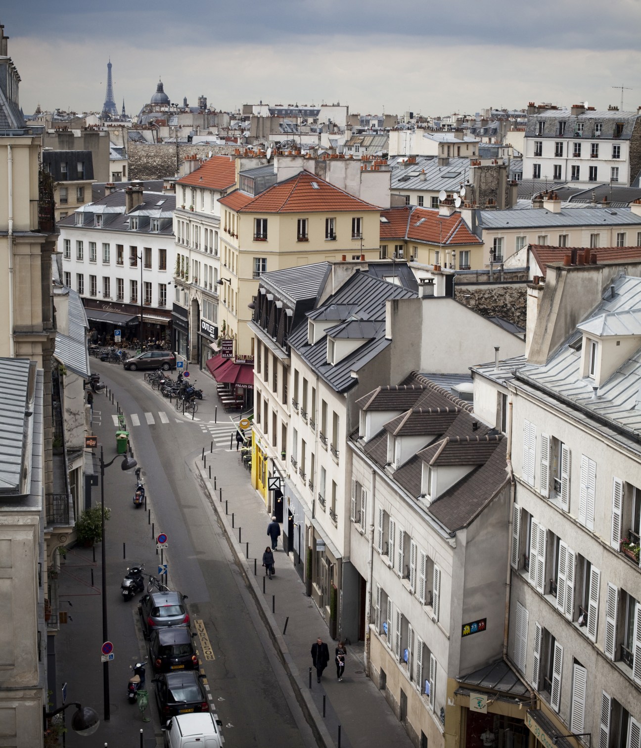 Aerial view of Rue de Charonne in Paris's 11th arrondissement showing historic buildings with distinctive rooftops and the Eiffel Tower in the distance.