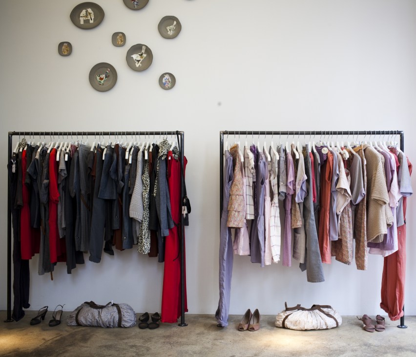 Interior of Sessùn boutique showing two clothing racks with womenswear and decorative plates on white wall.