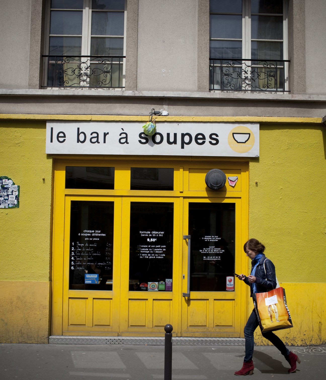 Bright yellow storefront of Le Bar à Soupes with a woman walking past carrying a yellow shopping bag.