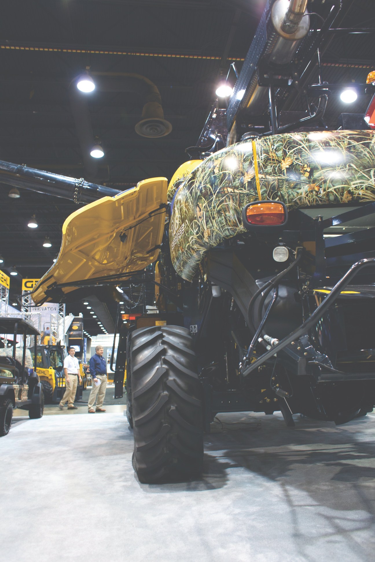 A yellow and black tractor with camouflage-patterned body displayed at an indoor farm machinery exhibition.