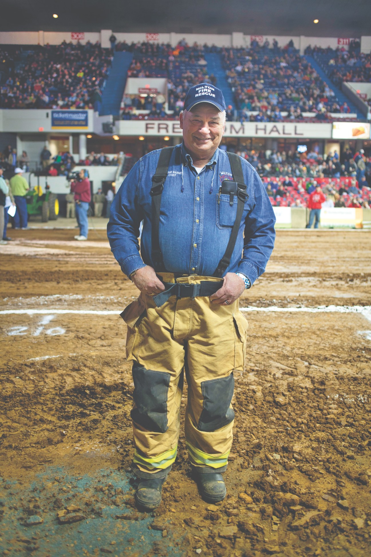 Fireman in protective gear standing on dirt arena floor at Freedom Hall during tractor pull event.