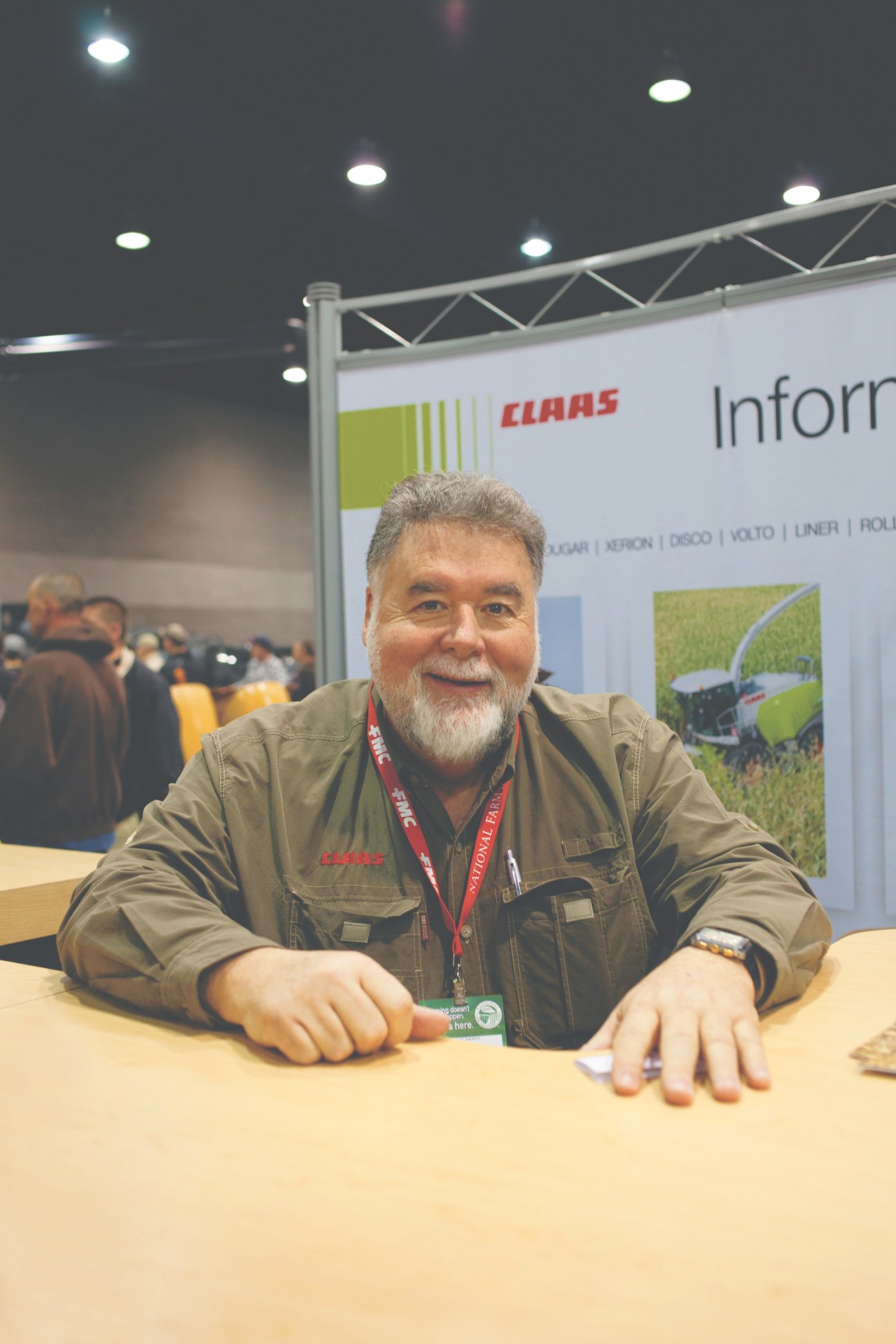 Mike Gibbons of Claas at the National Farm Machinery Show booth wearing tan work shirt and red credential badge.