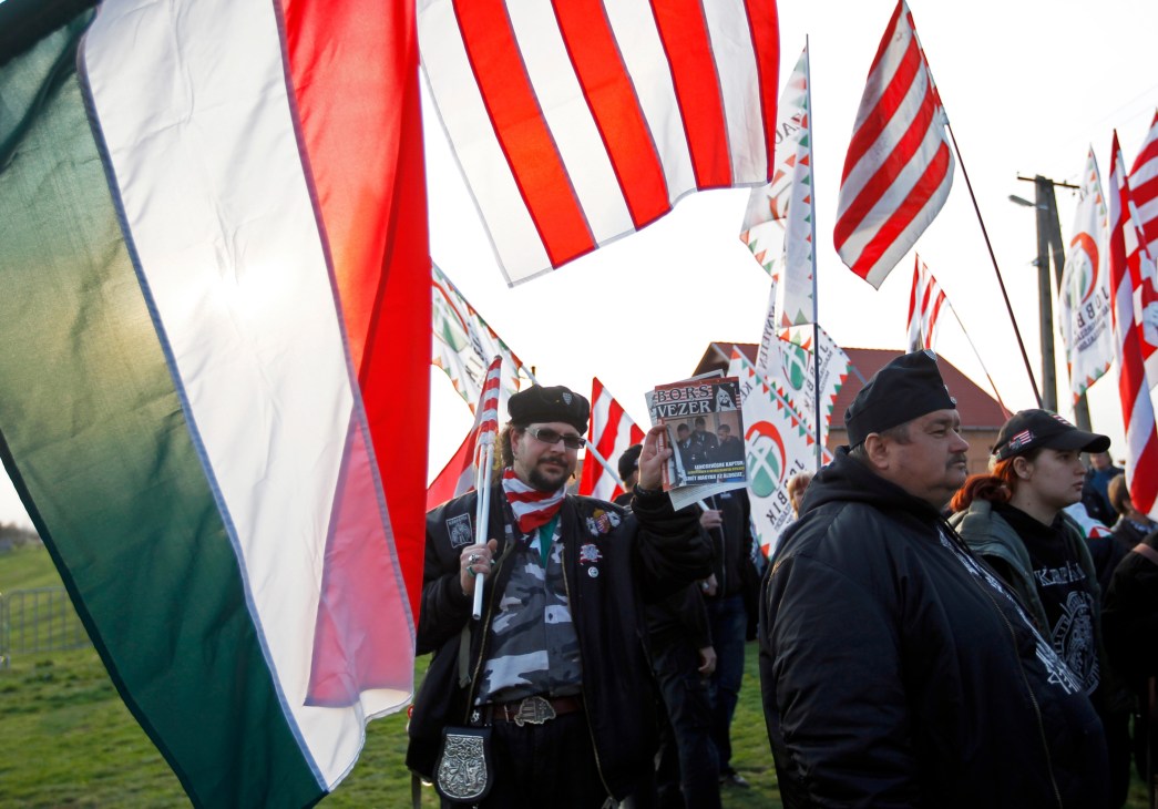 Far-right Jobbik supporters hold Hungarian flags and signs at a political rally.