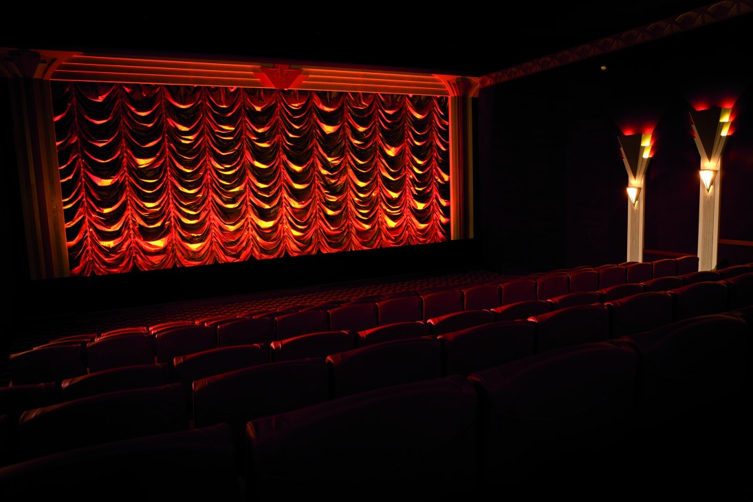 Art Deco cinema interior with red velvet curtains, neon-lit stage frame, and rows of red seats at The Roxy.