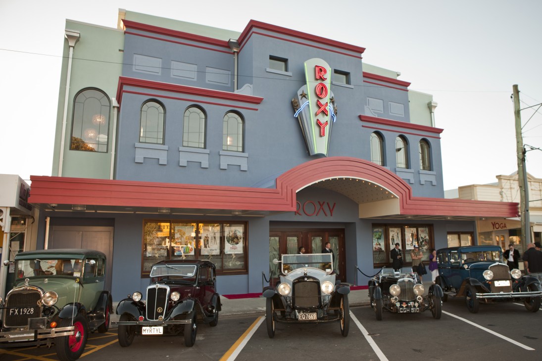 The Roxy 3D cinema in Wellington, an Art Deco building painted blue and red with vintage cars parked outside.