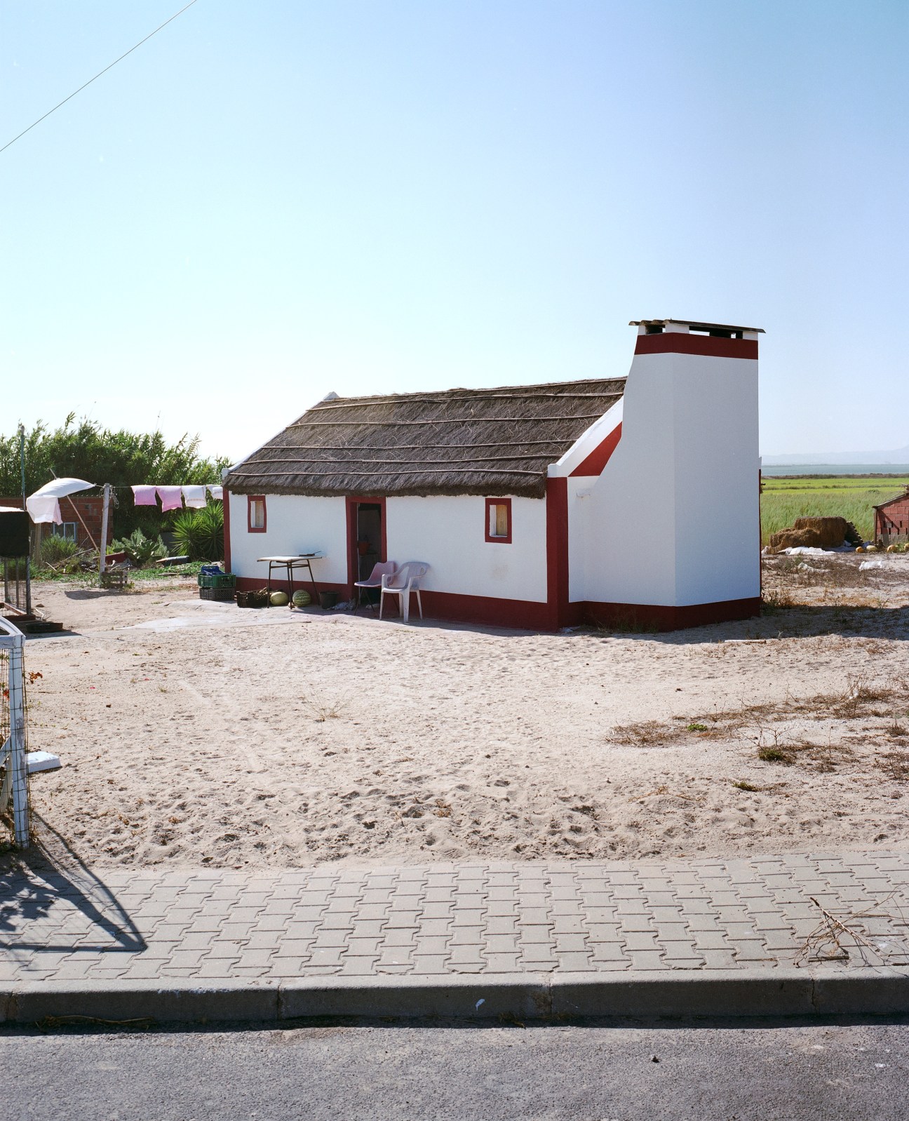 Traditional white and red fisherman's house with thatched reed roof in sandy Comporta landscape.