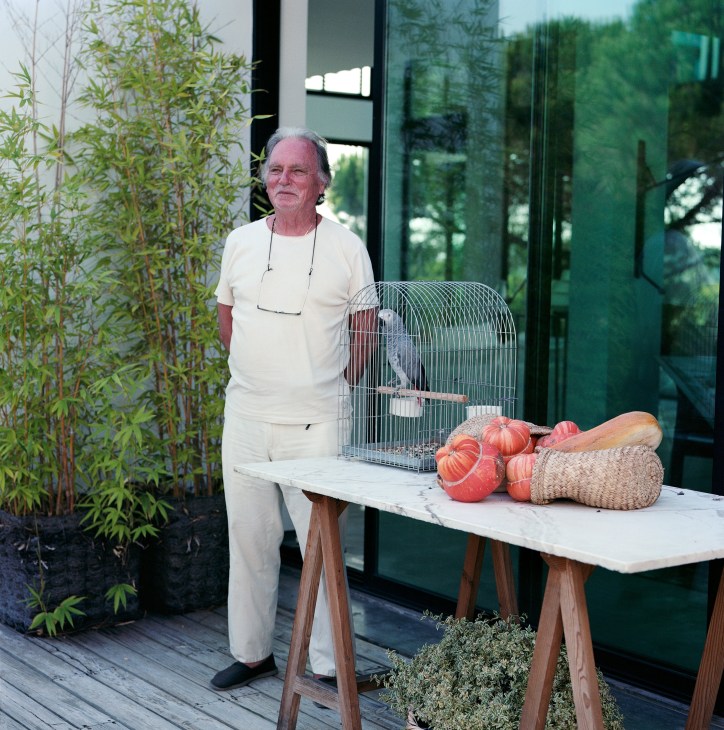 Architect Pedro Ferreira Pinto stands on a wooden deck beside a table with red tomatoes and a birdcage.