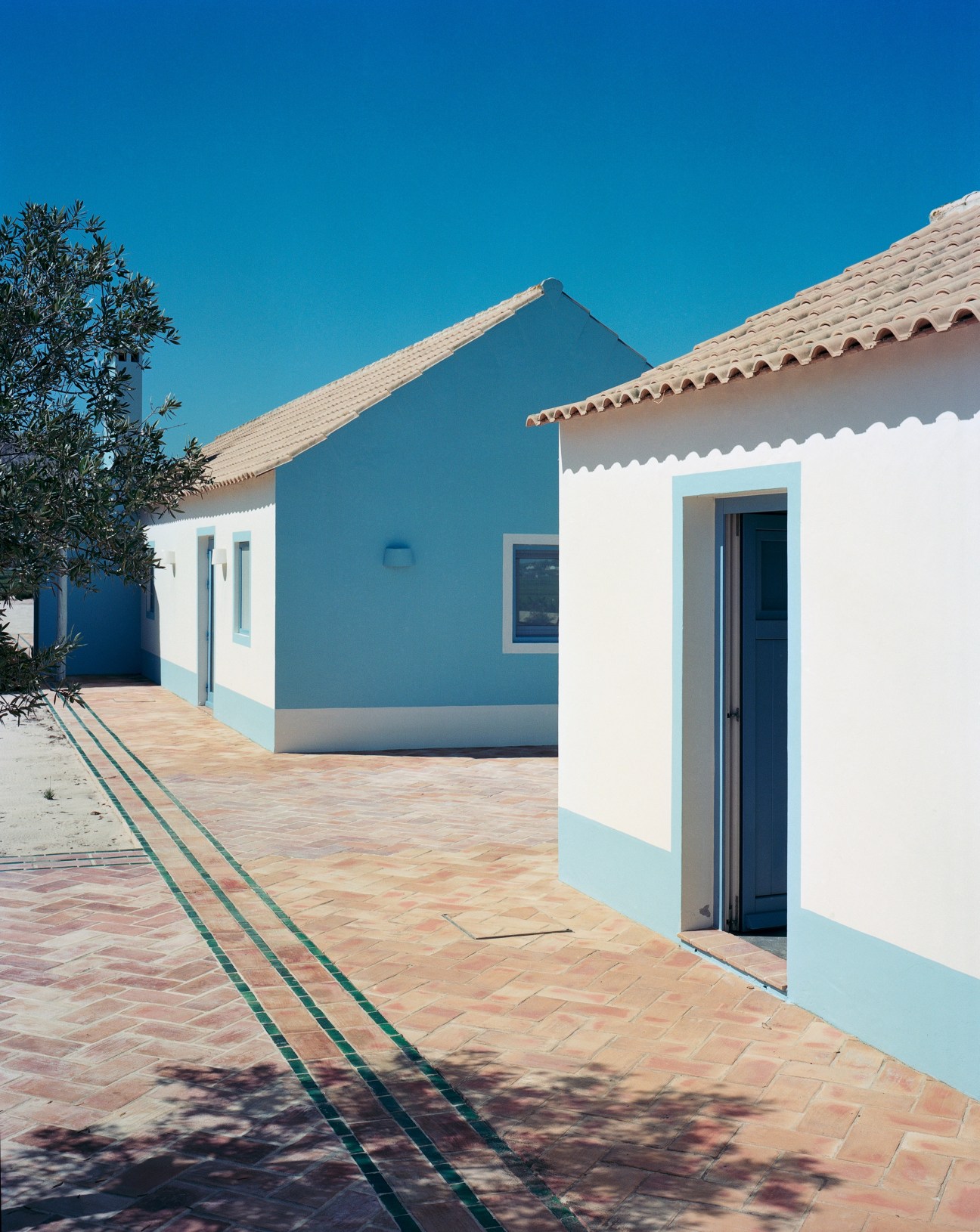 Blue and white houses with tiled roofs and terracotta courtyard in Comporta, Portugal.