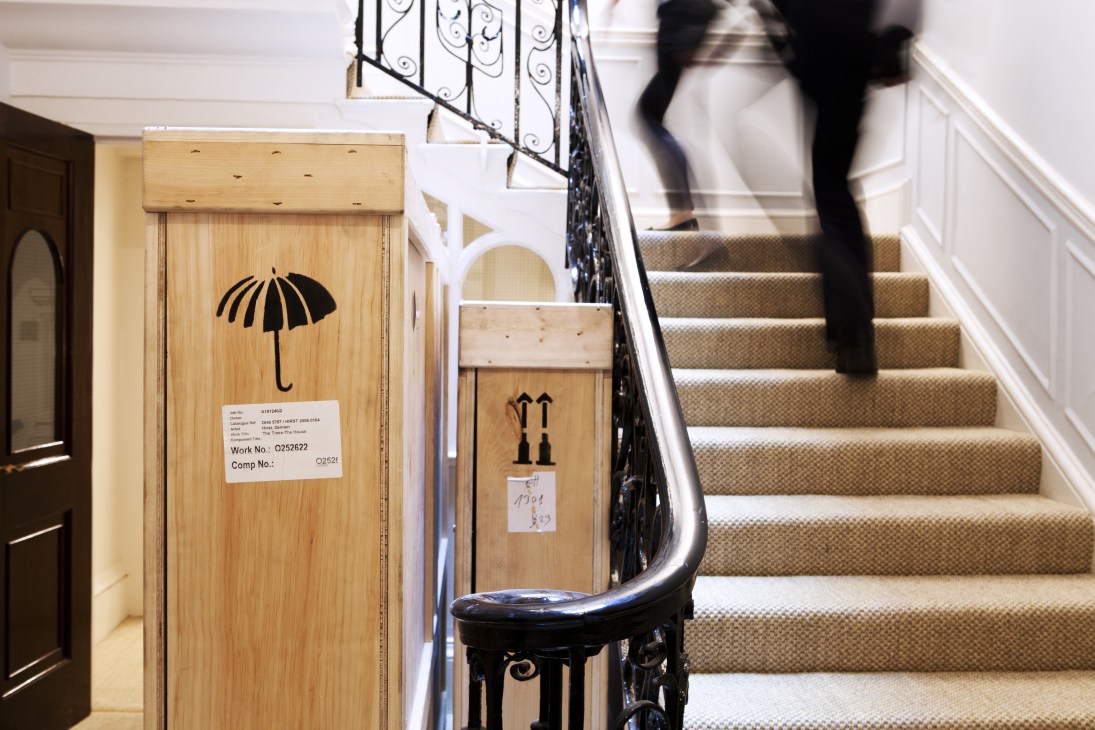 Wooden crates with umbrella symbols and shipping labels stacked on a staircase in a gallery.