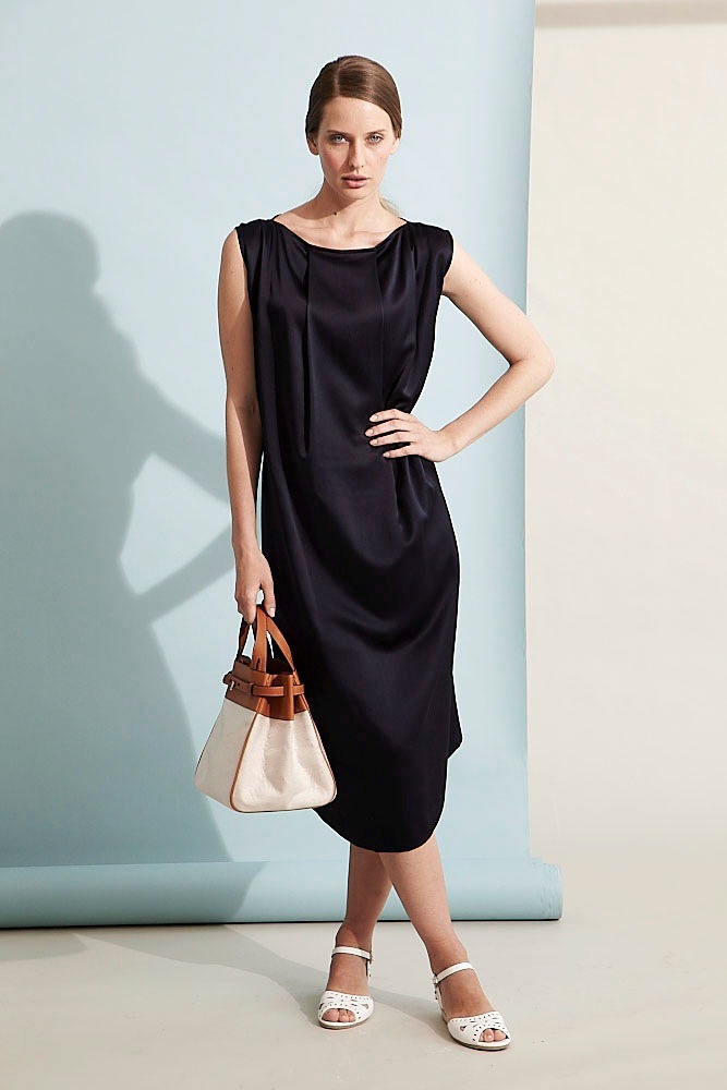 Woman wearing black sleeveless silk dress with brown and cream handbag and white sandals.