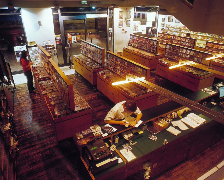 The Third Ear rental store interior with red display cases holding DVDs and an employee organizing inventory.