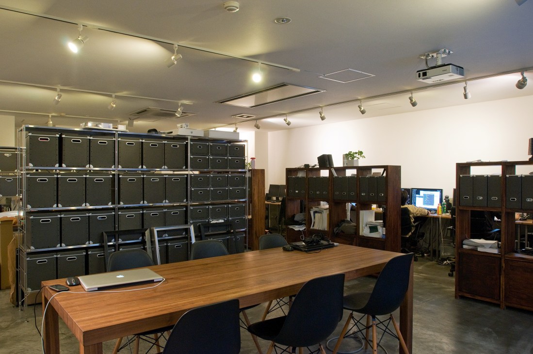 Interior of THA design office near Shibuya station with wooden desk, black chairs, and wall storage.