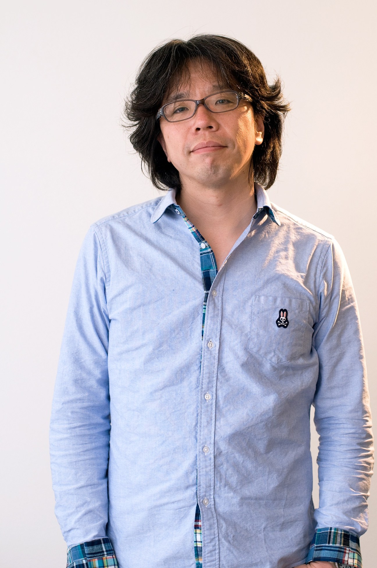 Portrait of Yugo Nakamura, a Japanese web and digital graphic designer, wearing glasses and a light blue shirt.