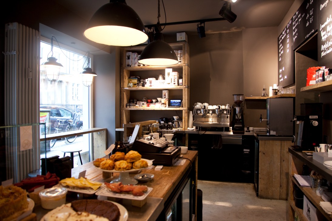 The Barn café interior in Berlin with wooden counter, pendant lights, shelving, and pastries on display.