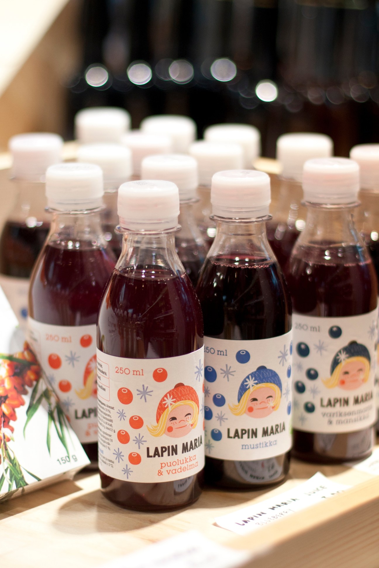 Bottles of Lapin Maria berry juice with illustrated labels displayed on a wooden surface.