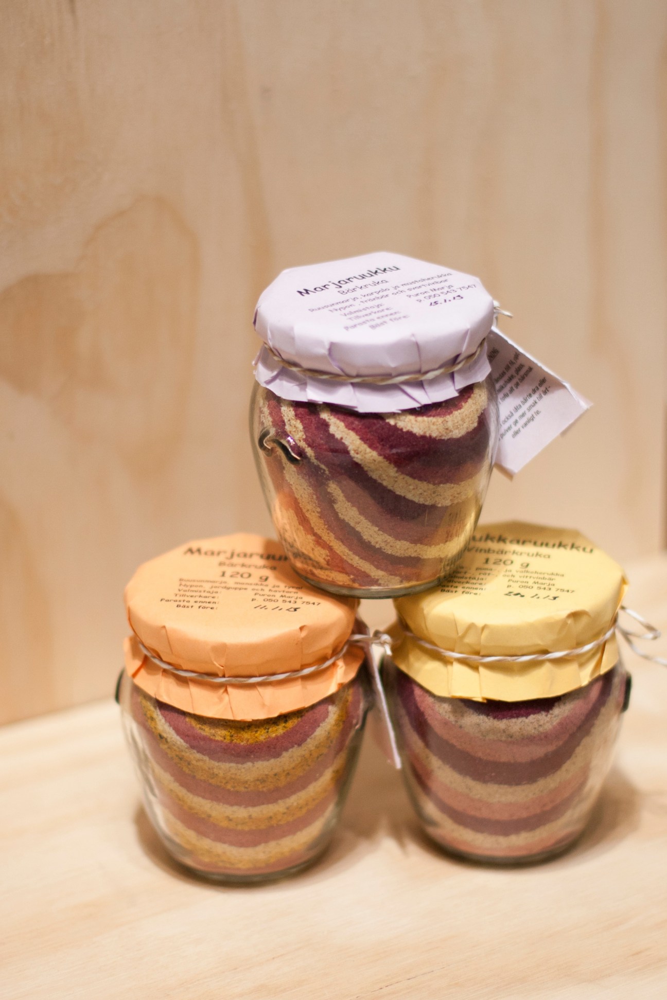 Three glass jars with layered contents and paper labels, displayed in a pyramid arrangement against a beige background.