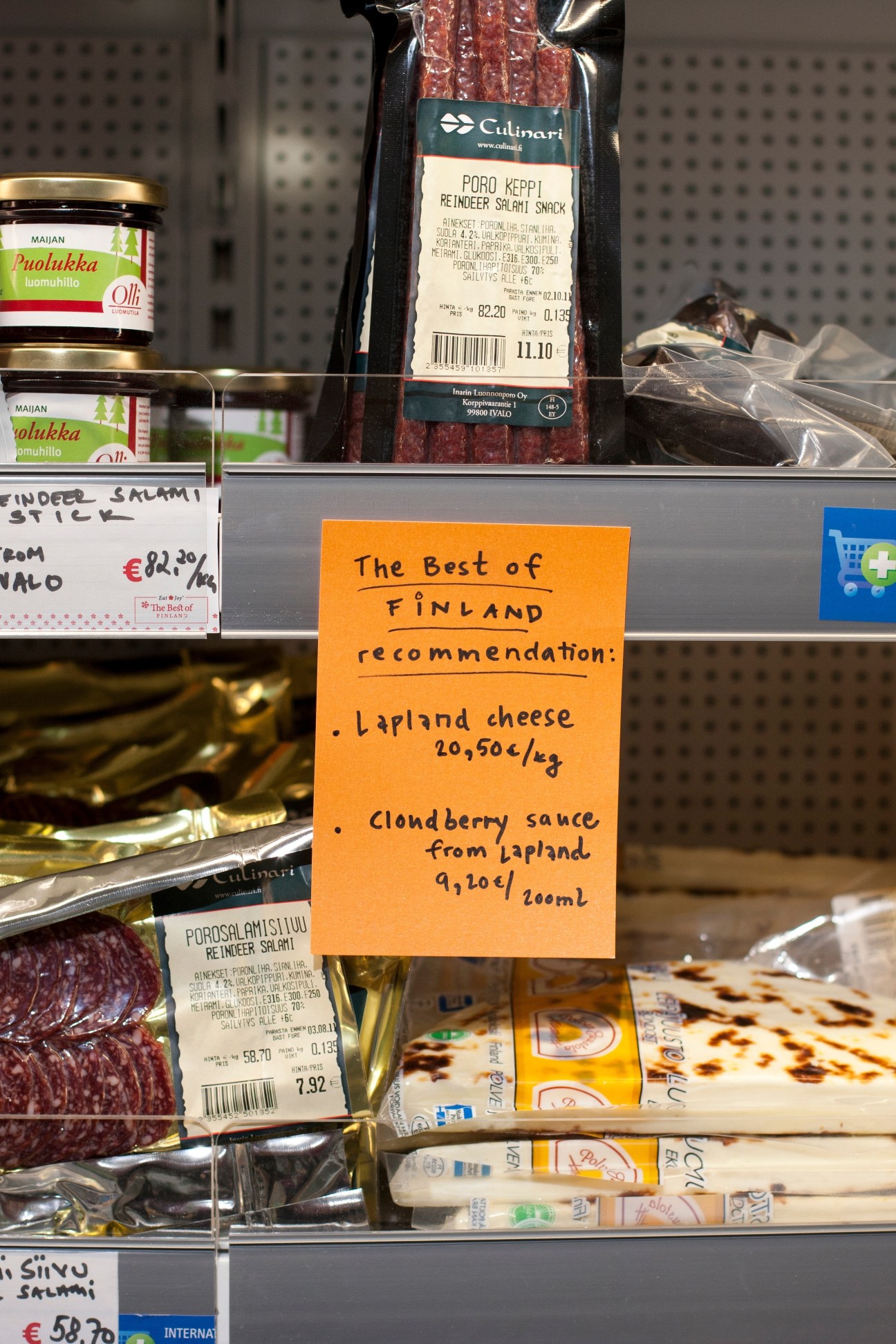 Best in Finland shop display with Finnish products including reindeer salami, cheese, and berry sauce with handwritten orange recommendation sign.