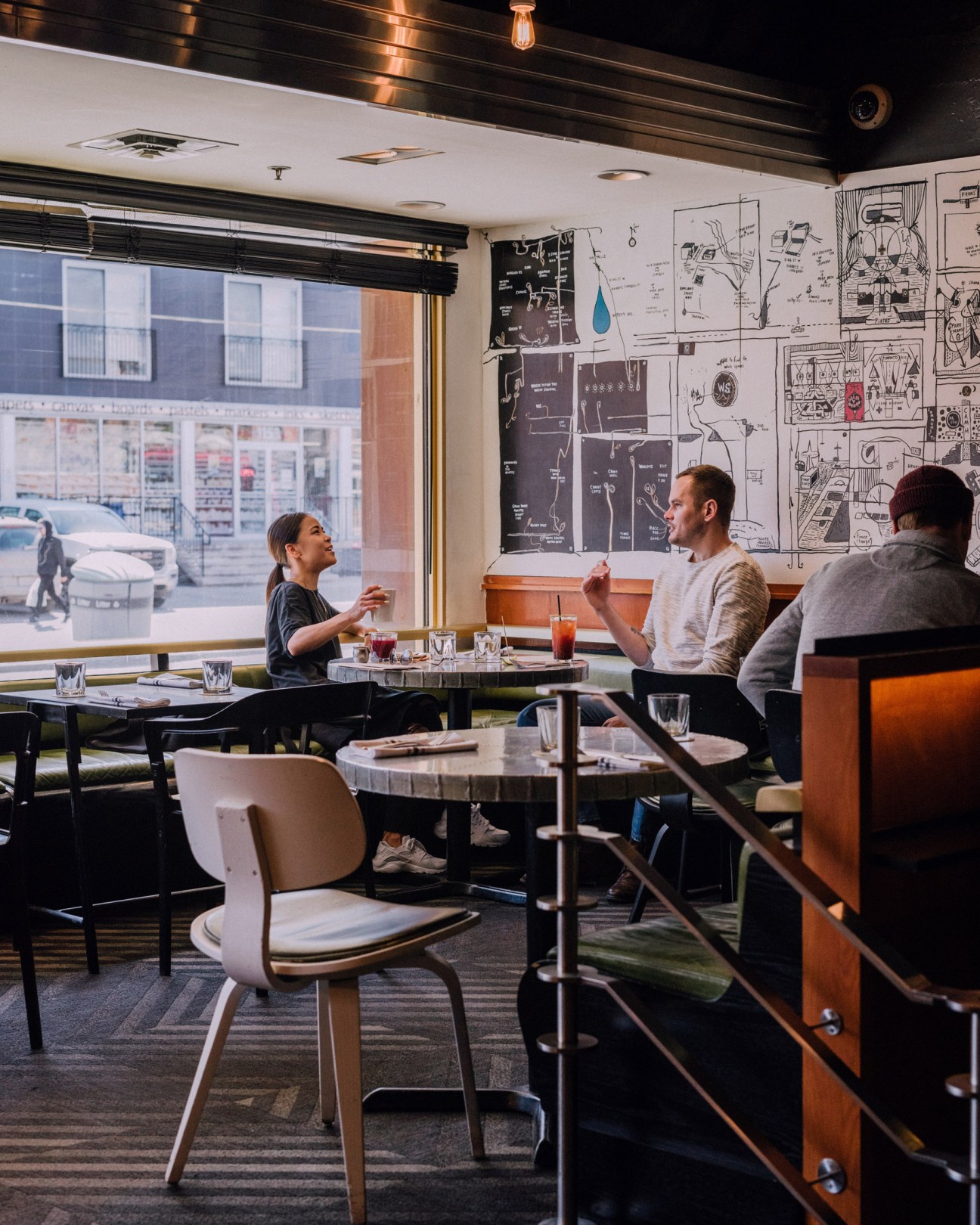 People chatting at a table in the Drake Hotel dining room with street views and architectural drawings on the wall.