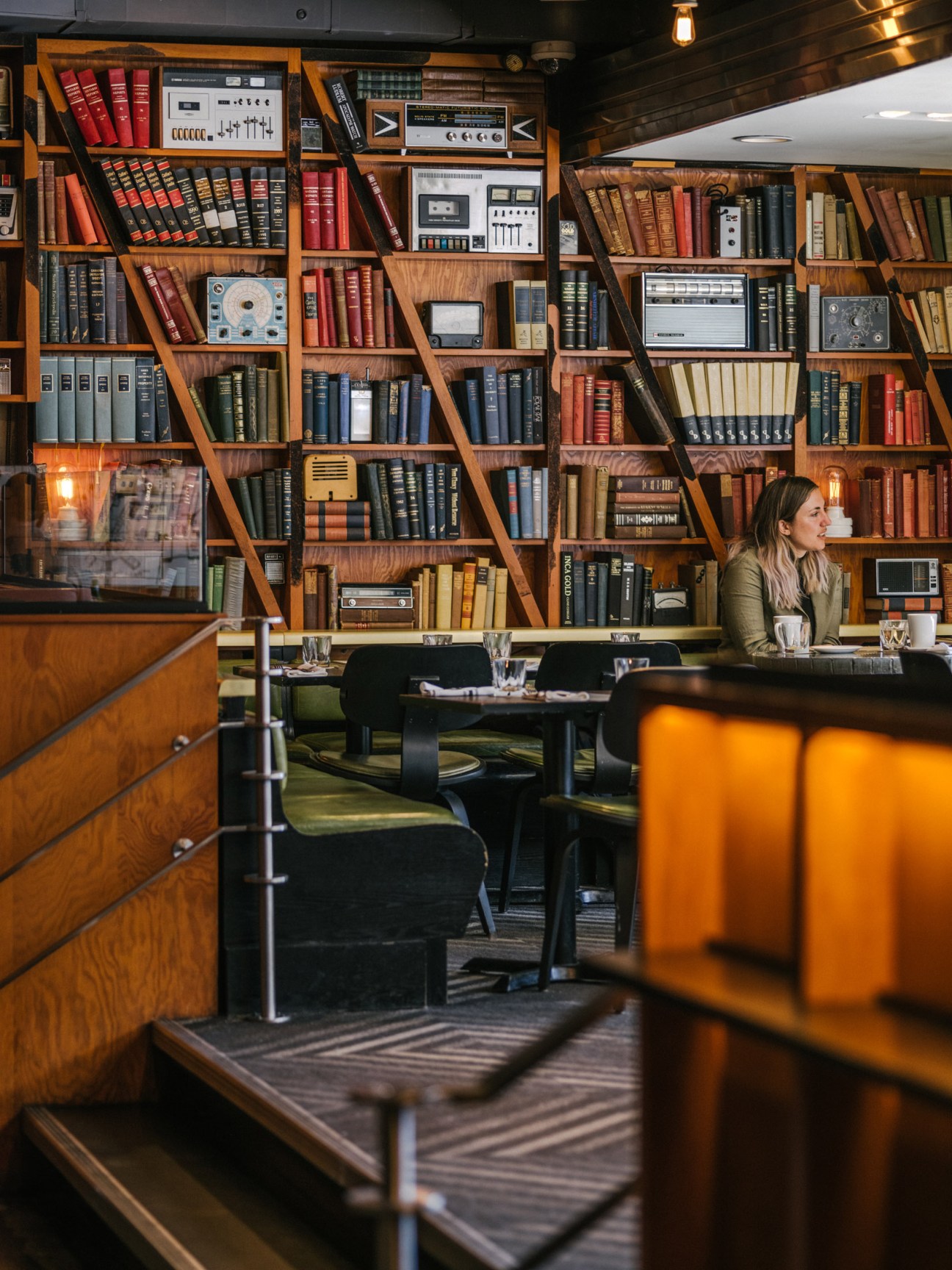 Drake Hotel dining room with woman seated at table before wall of vintage books and radios.