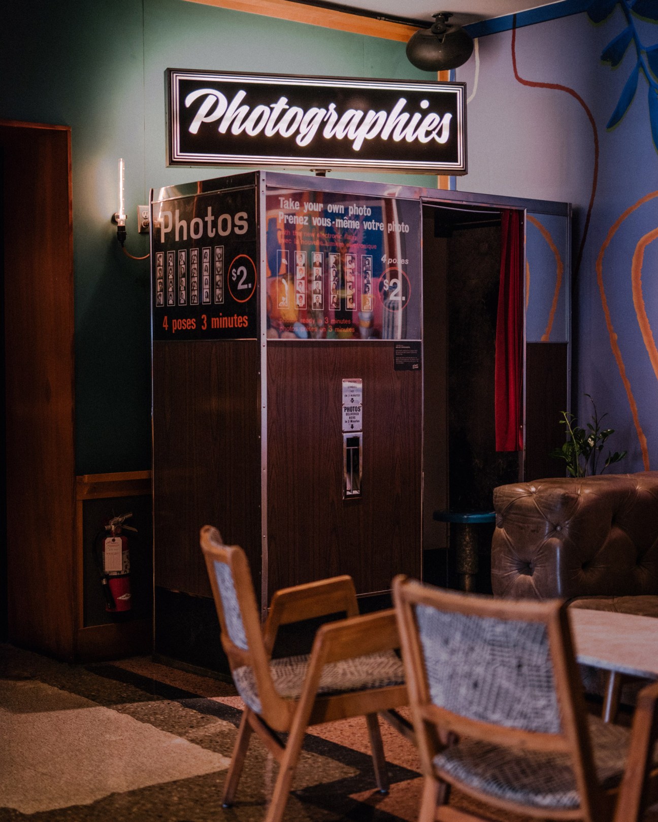 Vintage photo booth in The Drake Hotel lobby with neon sign above and mid-century chairs in foreground.