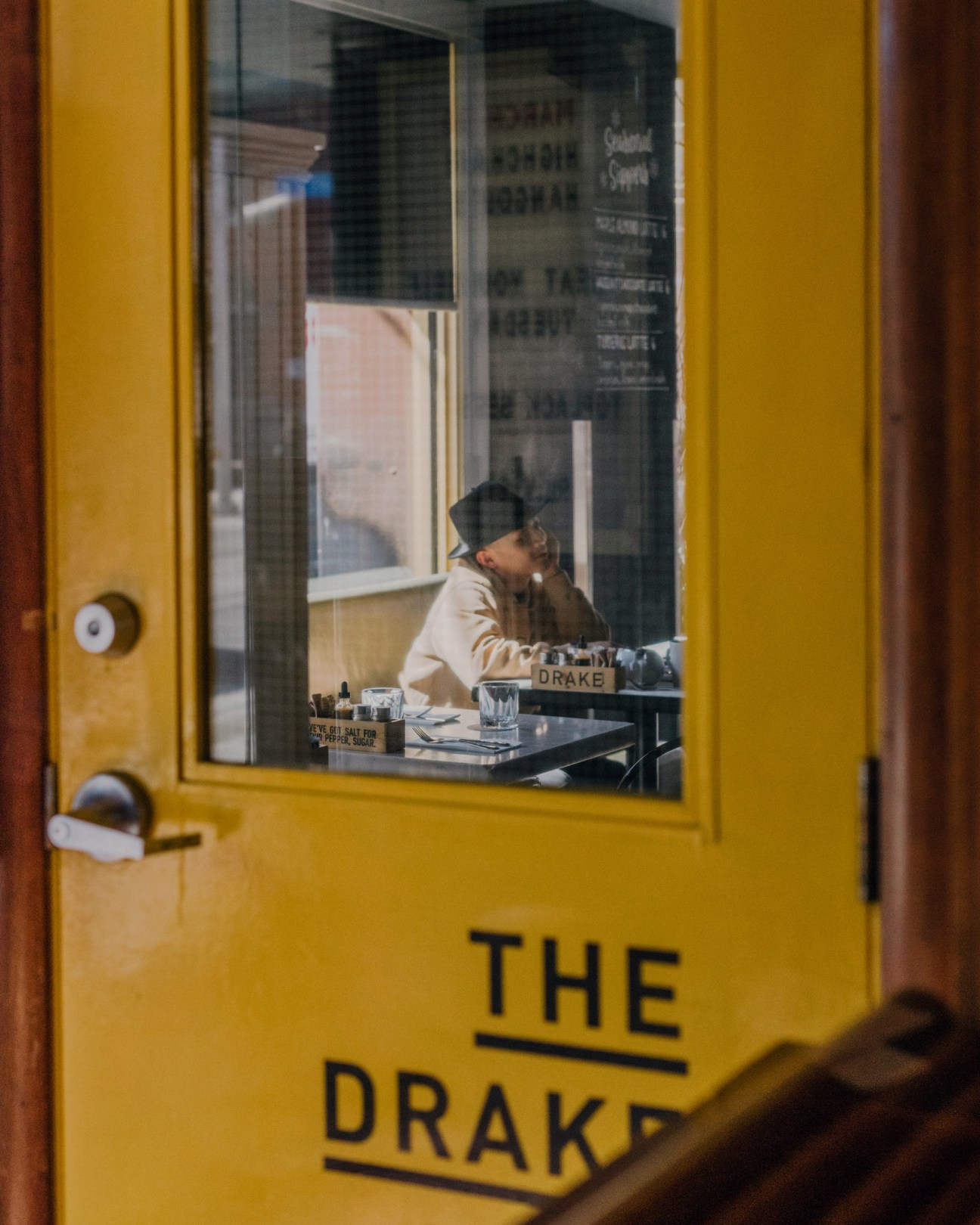 Person seated at a table inside The Drake Hotel, visible through the bright yellow entrance door.