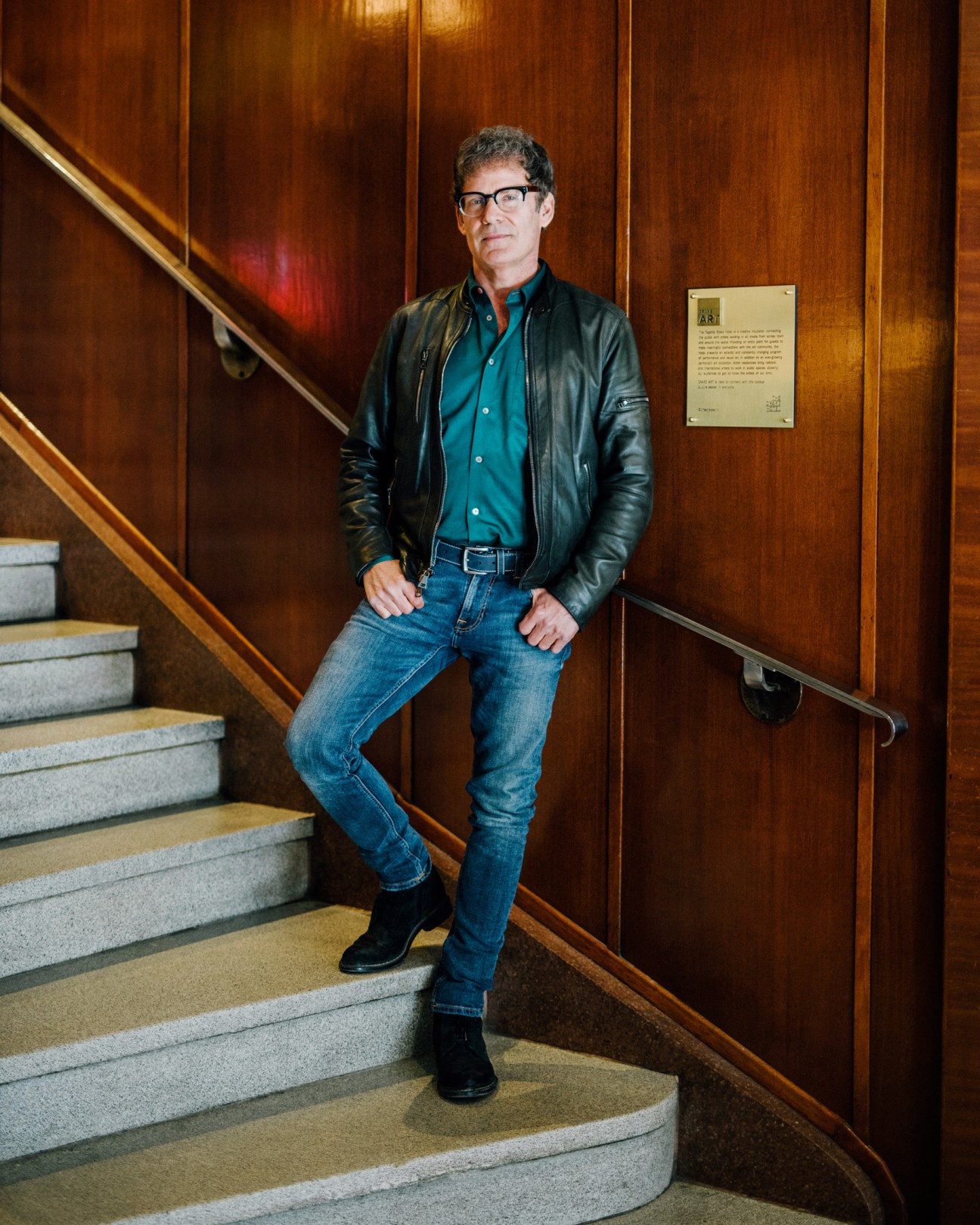 Jeff Stober, founder of the Drake Hotel, standing on wooden stairs against a wood-paneled wall.