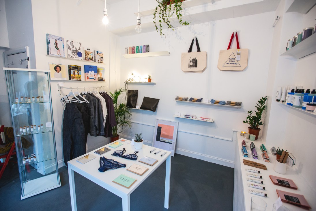 Thethestore retail shop interior in London featuring clothing racks, shelves with magazines and products, tote bags, and pendant lighting.