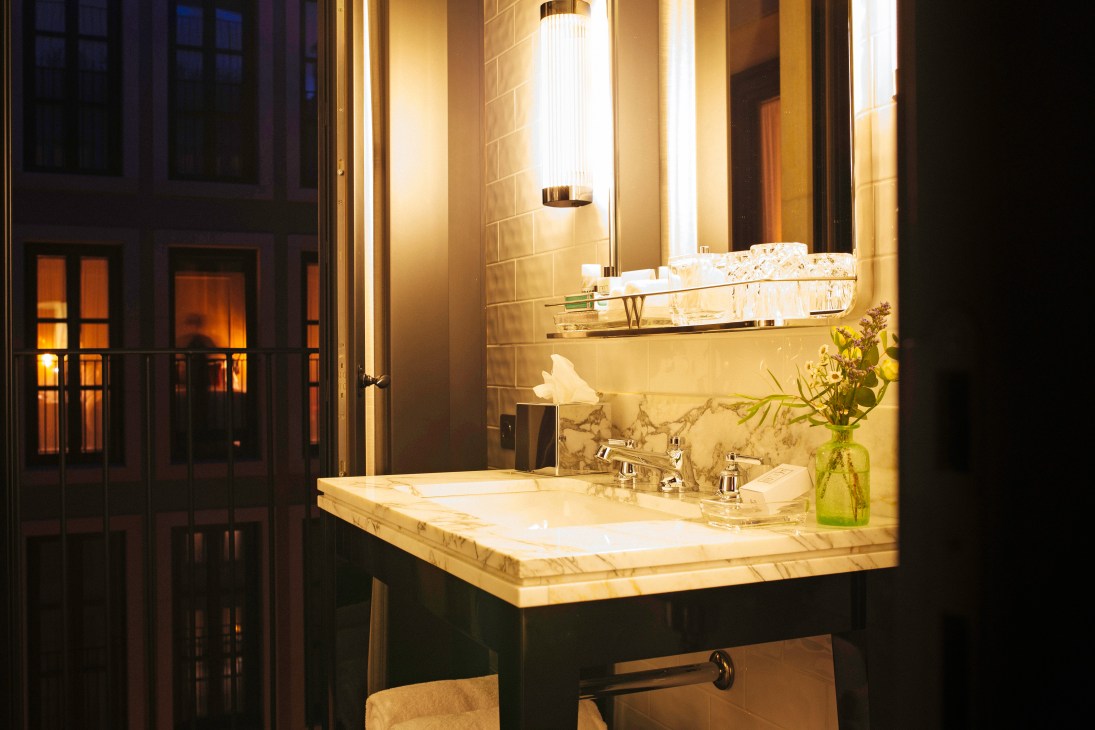 Hotel bathroom with marble countertop, illuminated mirror, and green flowers in a vase.
