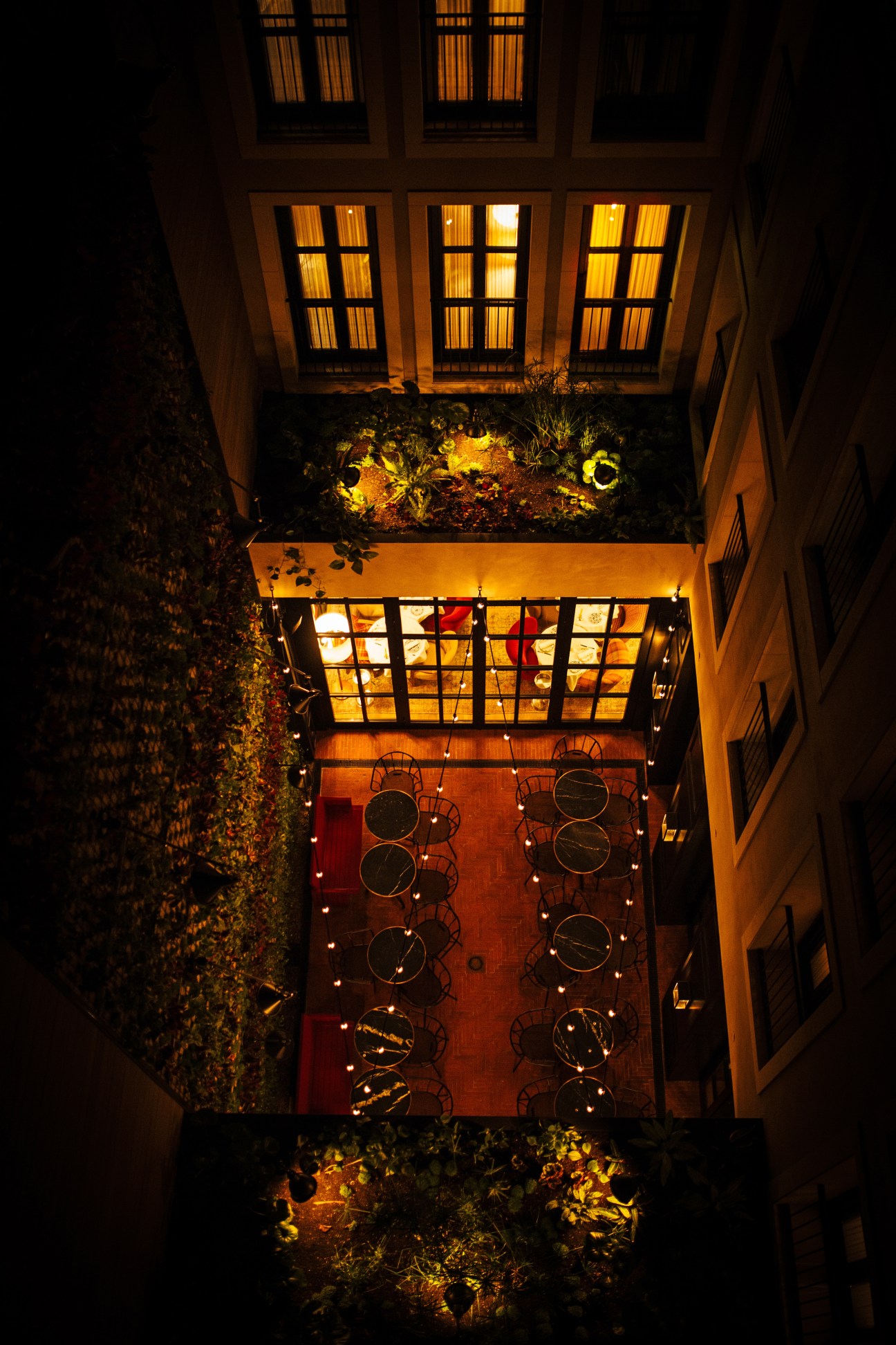 Overhead view of The Wittmore Hotel's courtyard with red-tiled floor, metal chairs, and illuminated windows above.