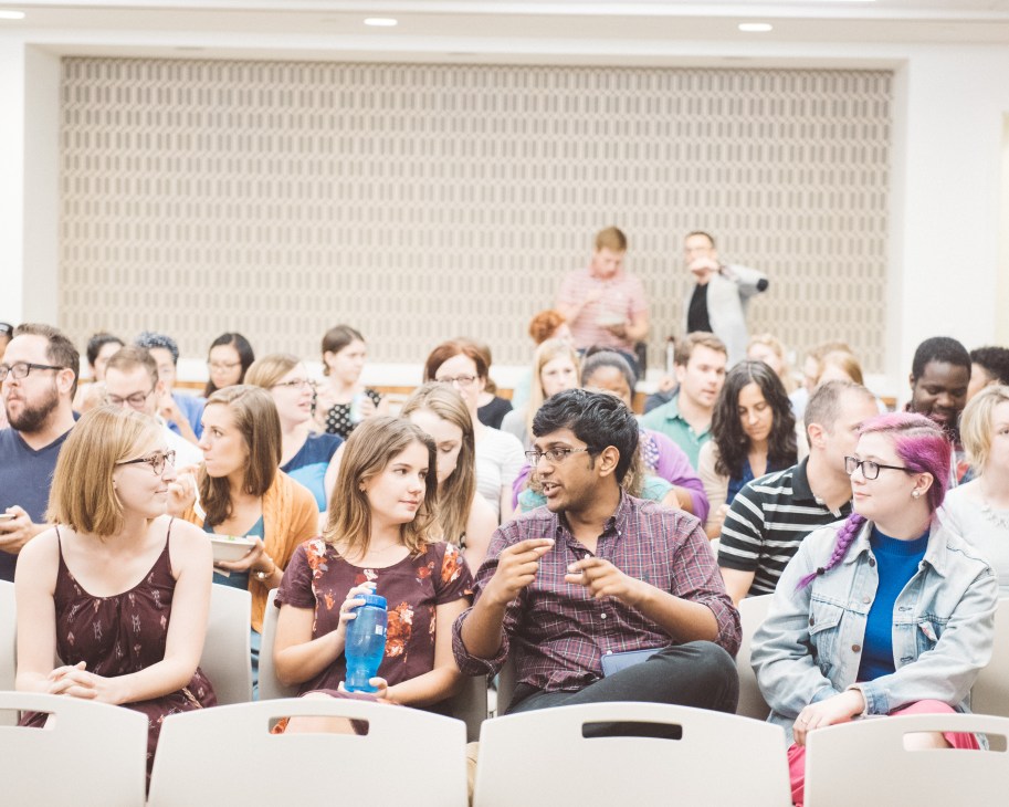 A diverse group of staff members seated in a large auditorium during a New America meeting.