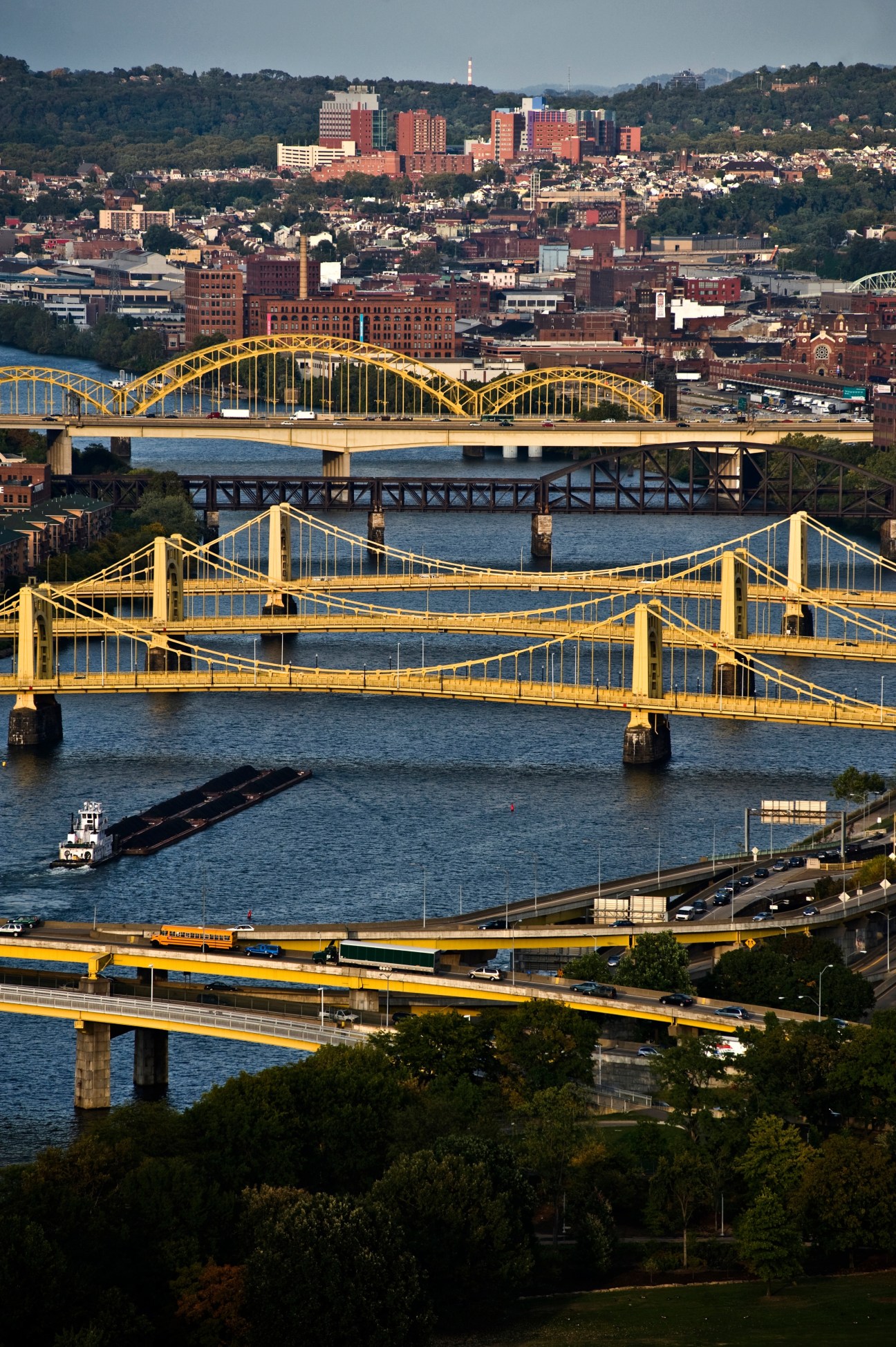 Pittsburgh skyline with yellow bridges spanning the river and dense urban buildings on hillside.