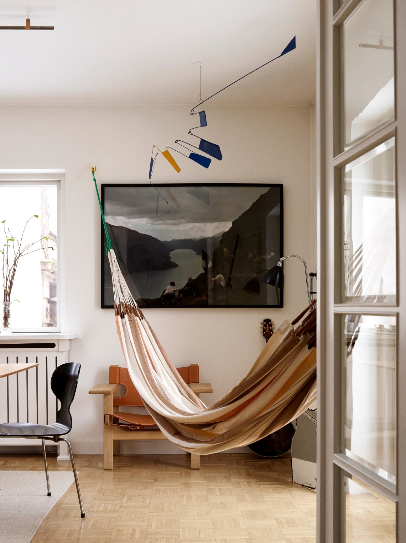 Interior room with fjord photograph artwork on wall, mobile by Ib Geertsen hanging above, hammock, and modern furniture.