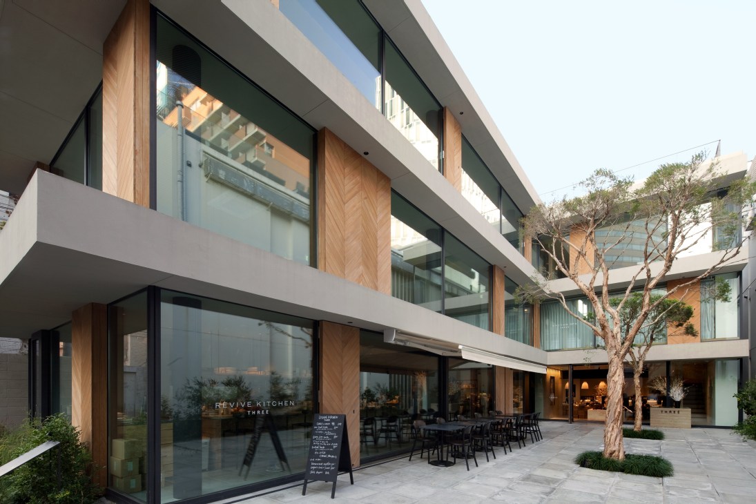 Three Aoyama cosmetics store and Revive Kitchen restaurant exterior featuring minimalist design with wooden and concrete elements in a courtyard setting.