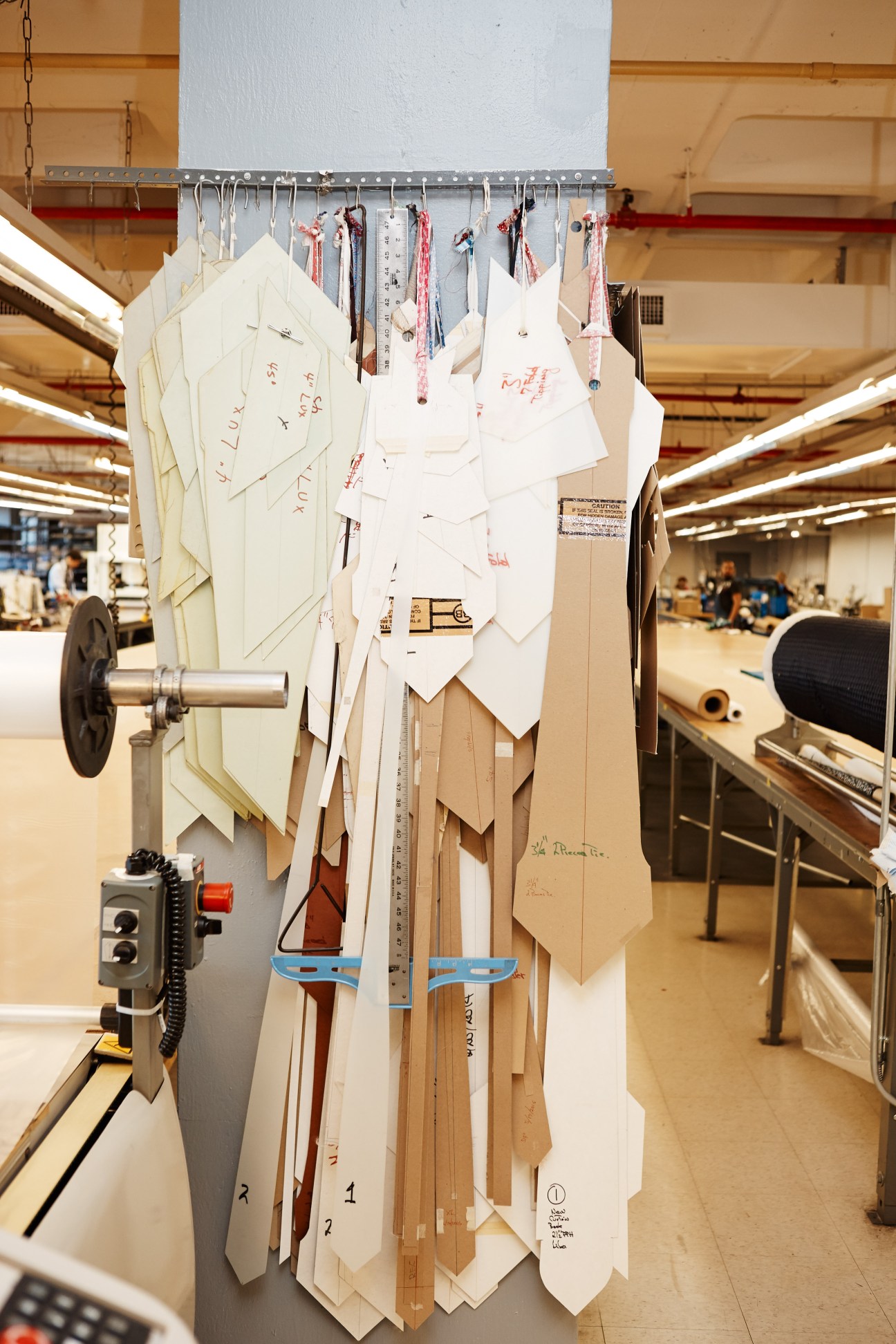 Clothing pattern samples and design sketches hanging from a rail in a factory setting.