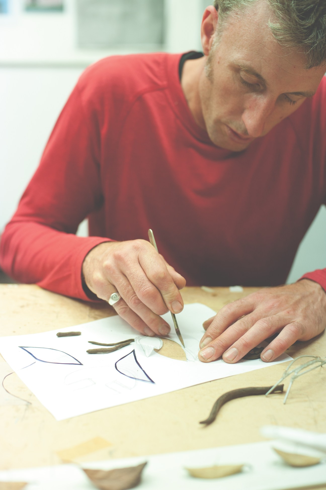Simon Hames, co-director of Izzat Design, works on a detailed design sketch with materials on a wooden table.
