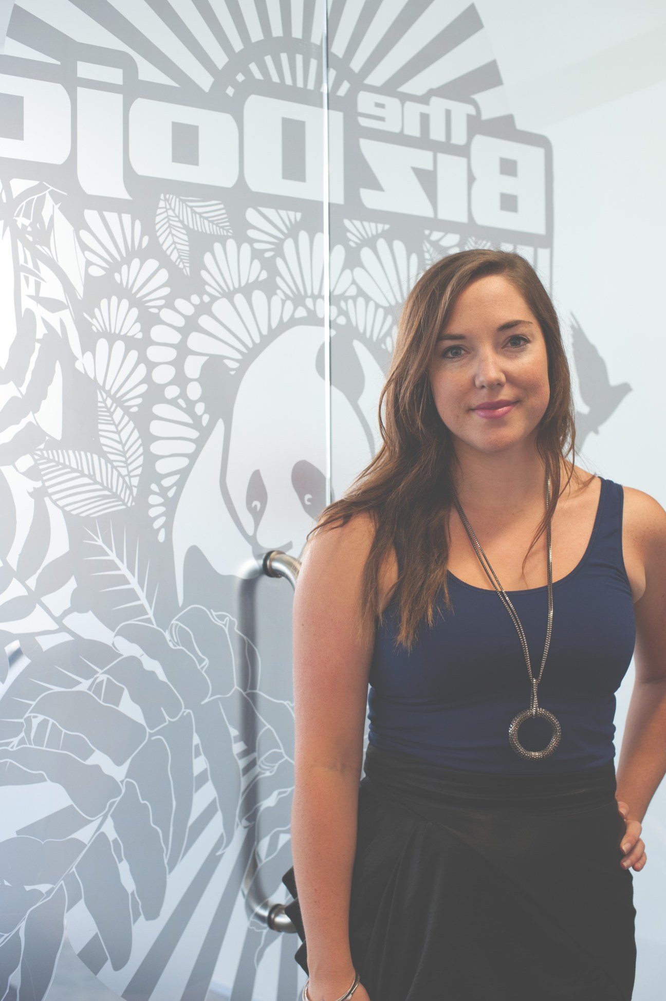 Katherine Field, community manager at BizDojo, stands in front of a frosted glass wall with the BizDojo logo and botanical design.
