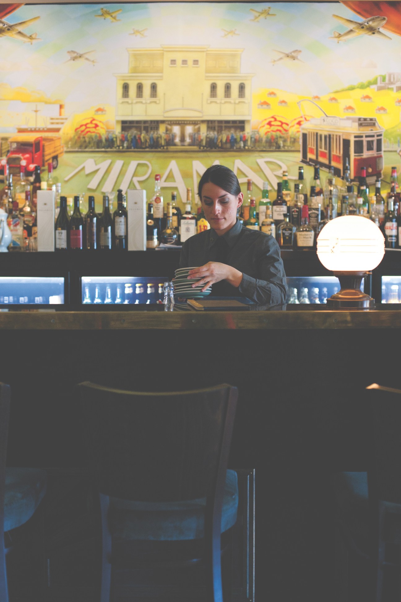 A female barista behind a counter at the Roxy Cinema, preparing drinks with a colorful mural backdrop.