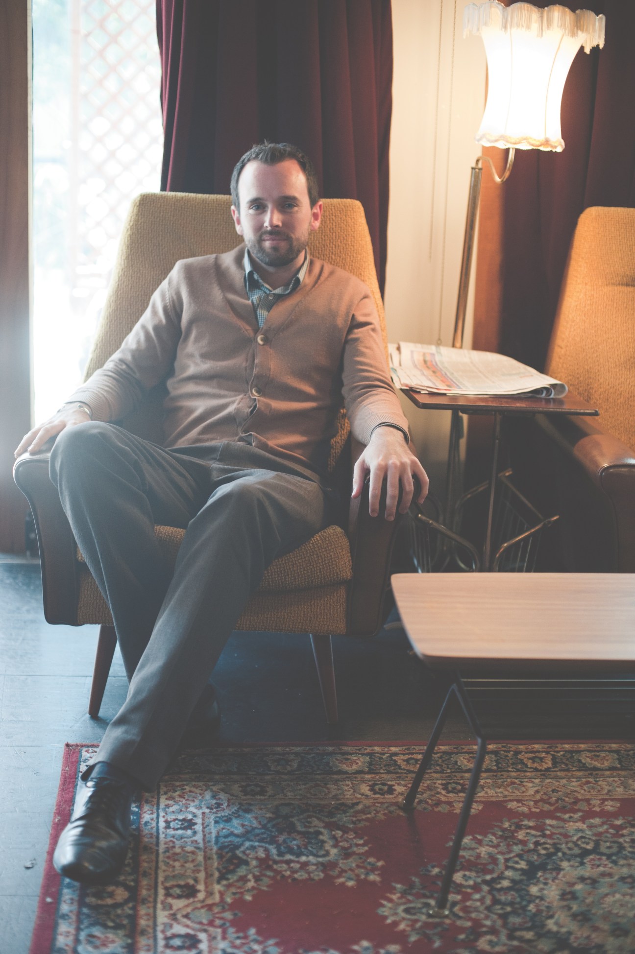 Jonny McKenzie, owner of Cuckoo Cocktail Emporium, sitting in an orange chair in a warmly-lit interior.