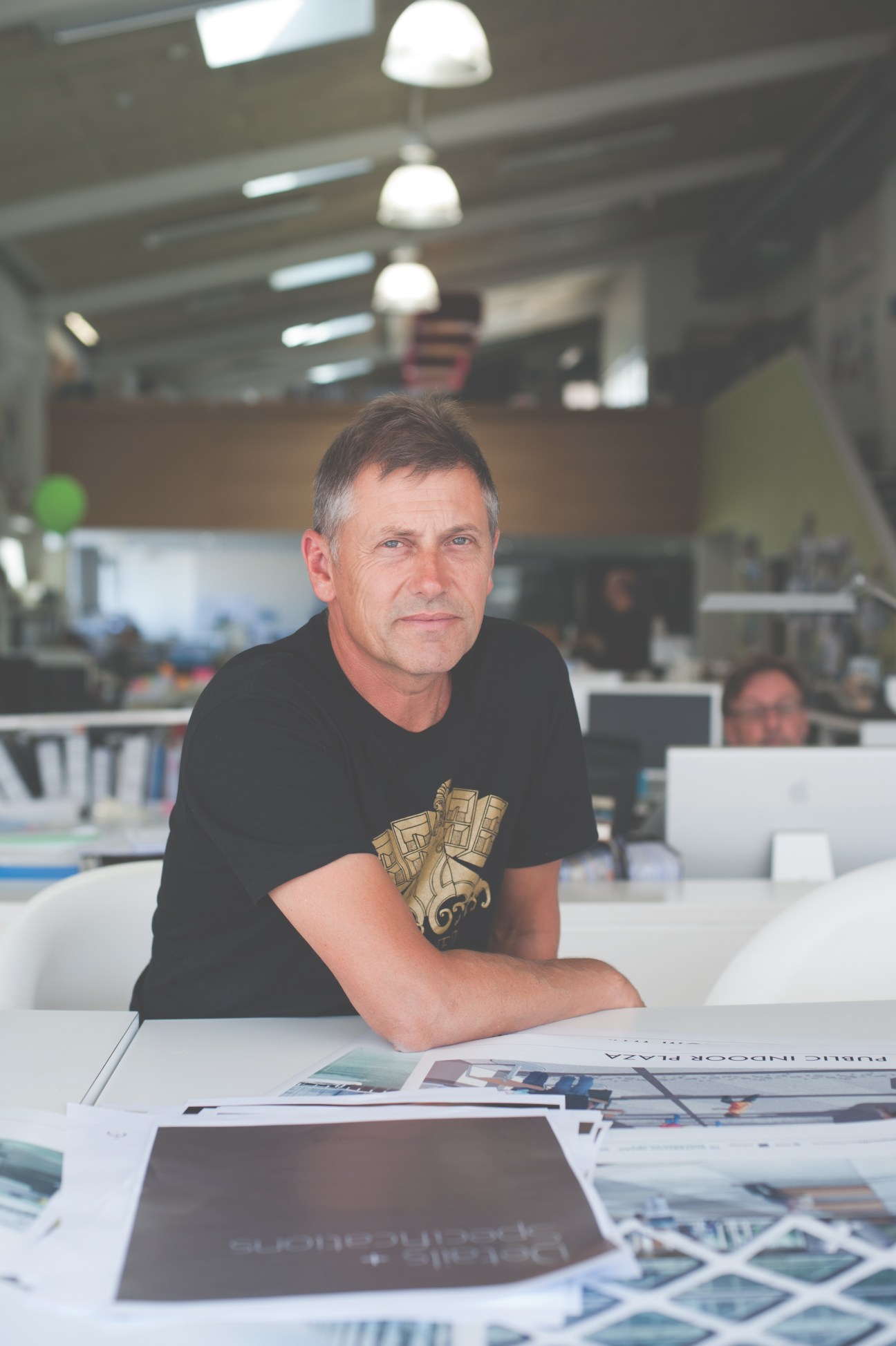 Nick Barratt-Boyes, director of Studio of Pacific Architecture, sits at a desk in a modern office space.