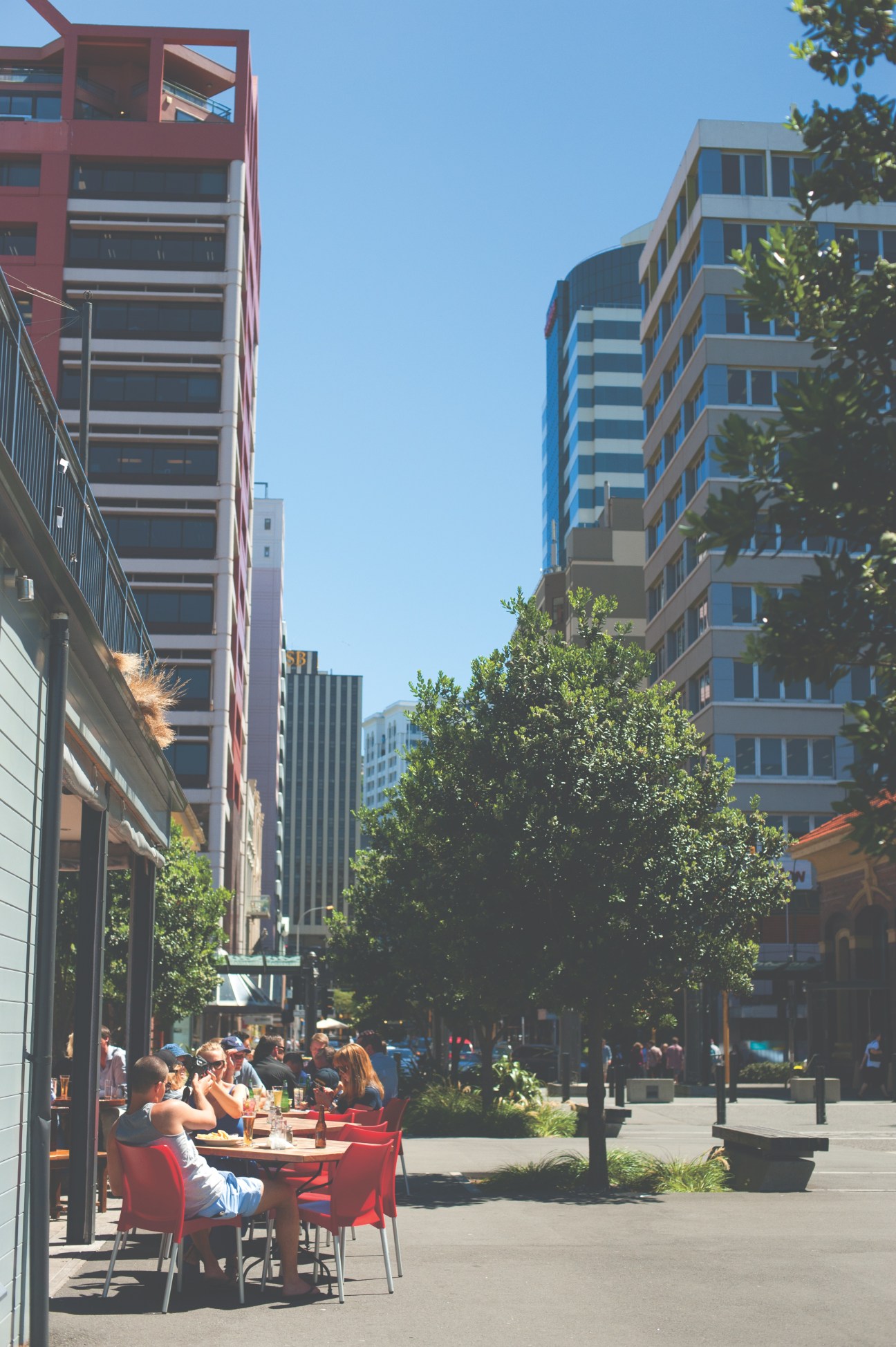 Wellington's waterfront plaza with modern buildings, outdoor seating, and pedestrians on a sunny day.