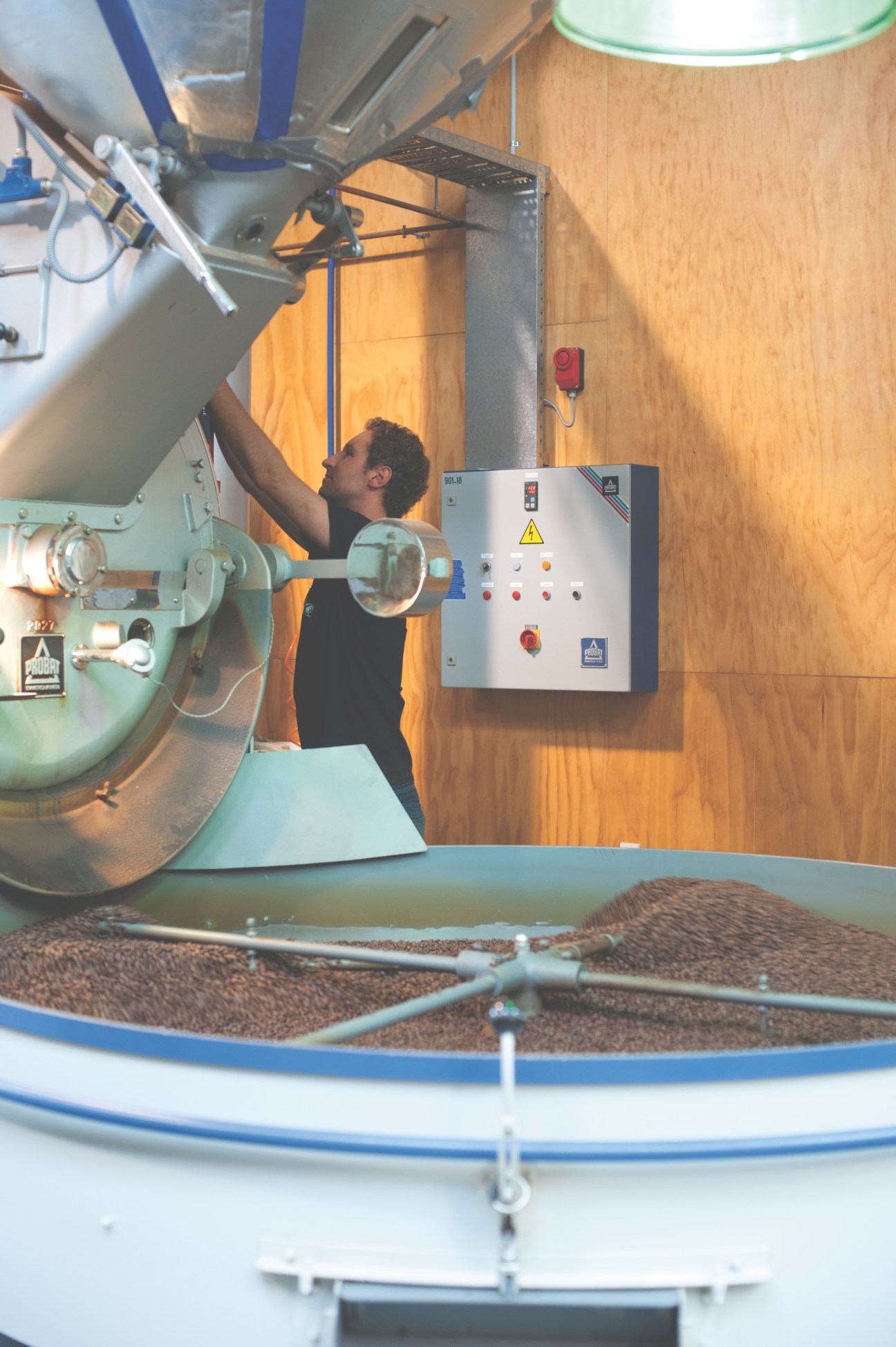 Worker roasting coffee beans in industrial roaster at Coffee Supreme facility.