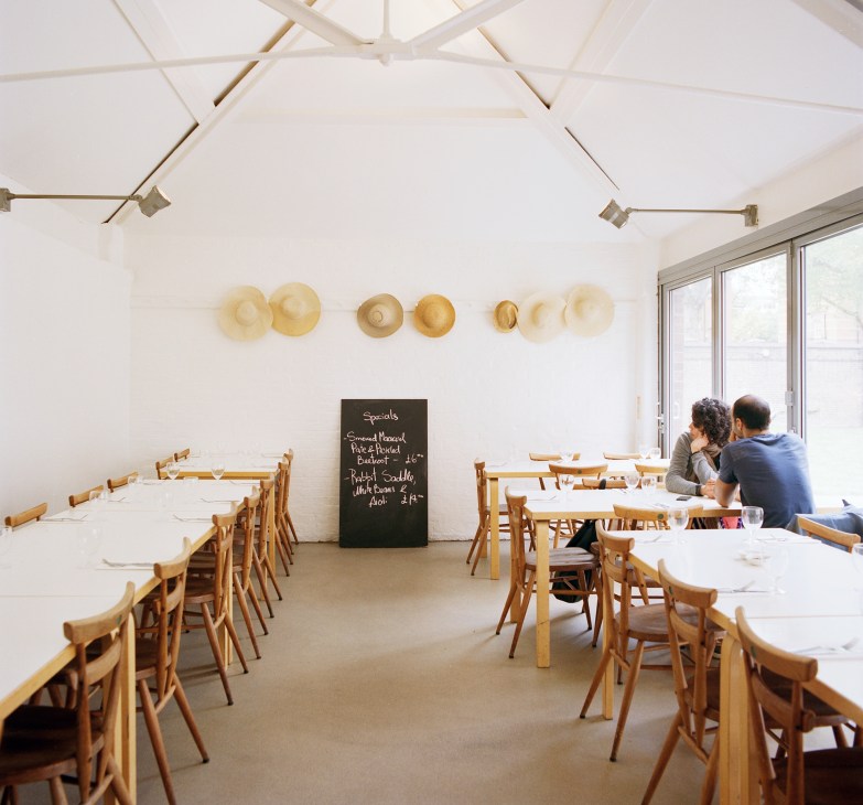Rochelle Canteen restaurant interior with wooden chairs, white tables, and specials board on wall.