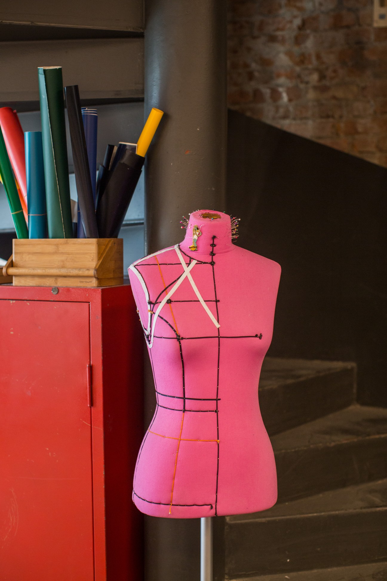 Pink dress form with measurement markings next to a red cabinet holding colored pencils and markers at Atolye co-working space.