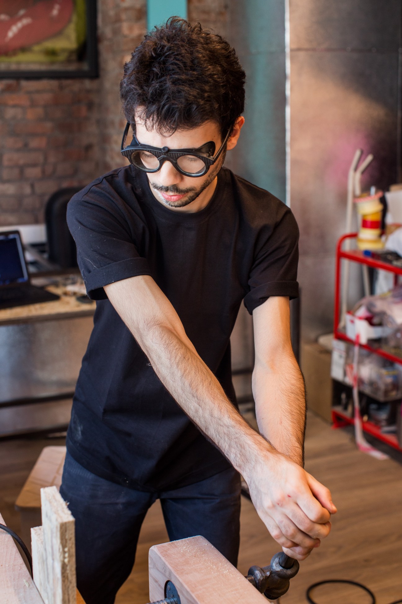 Man wearing glasses working with hand tools on wood in Atolye workshop.